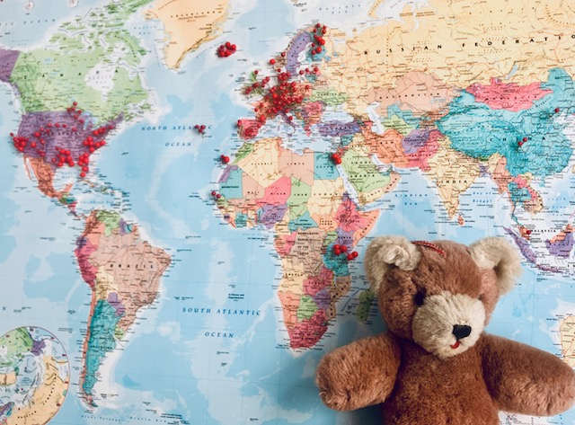 Weltkarte mit roten Markierungen, davor ein brauner Teddybär