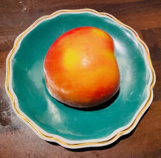 Ein halber, oranger Apfel auf einem altmodischen grünen Teller mit Goldrand auf einem braunen Holztisch