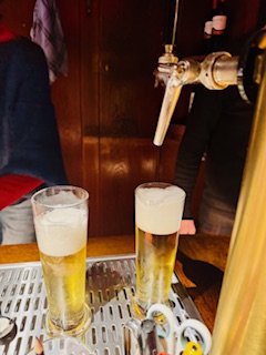 Metallischer Zapfhahn mit zwei halbvollen Biergläsern mit Schaum