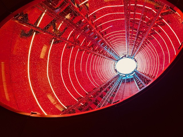 Blick nach oben in einen Aufzugsschacht der Battersea Power Station in London mit roten und gelben Neonlichtern und sichtbaren Schienen