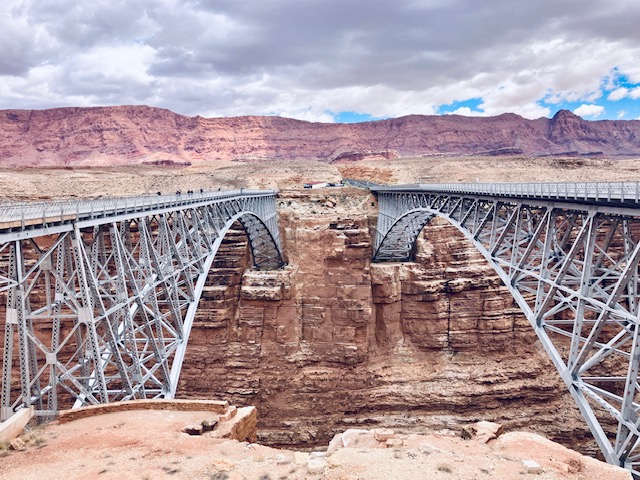 Zwei parallele Stahlbogenbrücken über eine tiefe Schlucht in einer felsigen Wüstenlandschaft