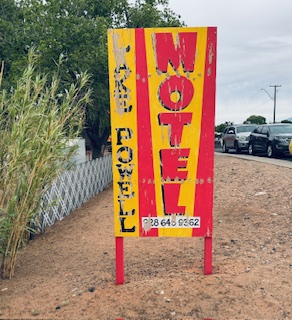 Altmodisches, verwittertes, gelb-rotes Schild mit der Aufschrift 'MOTEL' und 'Lake Powell' sowie einer Telefonnummer am Straßenrand