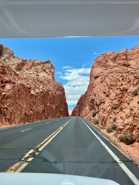 Straße führt durch eine rote Felsenschlucht in Utah unter blauem Himmel mit Wolken