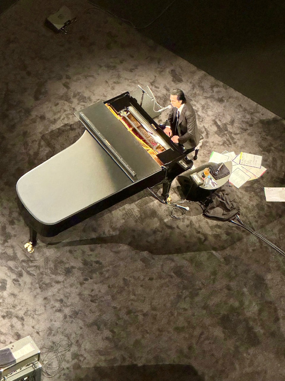 Mann in Anzug sitzt am Flügel, umgeben von Noten auf Teppichboden. Der Mann ist der australische Musiker Nick Cave.
