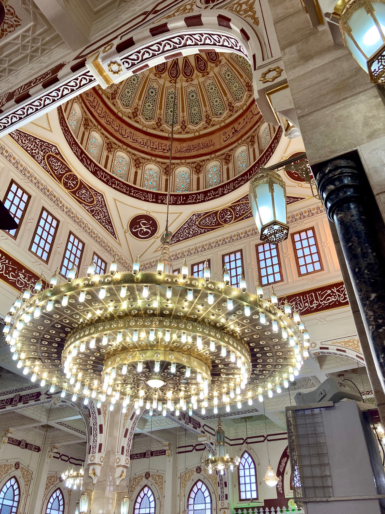 Innenraum der Moschee in Hurghada, Ägypten mit großem, rundem Kronleuchter und kunstvoll verzierter Kuppel mit arabischer Schrift