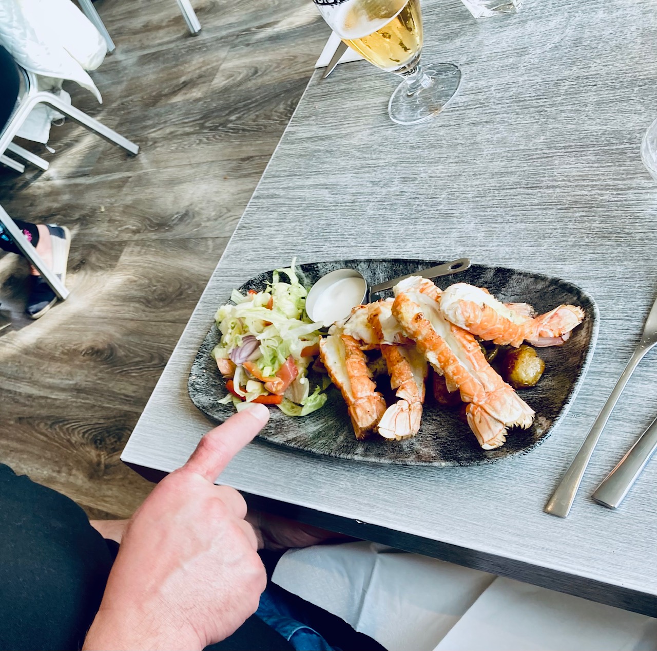 Teller mit Hummerschwänzen, Salat und Sauce auf einem Tisch in einem Restaurant, im Hintergrund ein halbvolles Glas Bier
