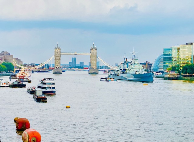 Blick auf die Tower Bridge in London mit mehreren Booten auf der Themse und modernen Gebäuden am Ufer