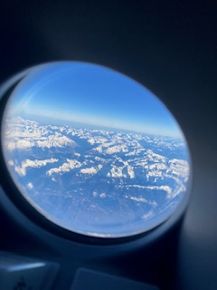 Blick aus einem runden Flugzeugfenster auf die verschneiten Pyrenäen