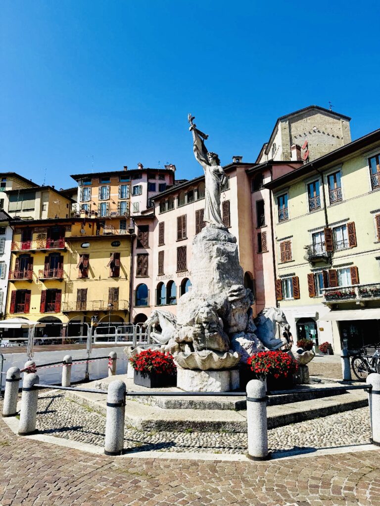 Ein großer Brunnen umgeben von historischen Häusern unter einem klaren blauen Himmel