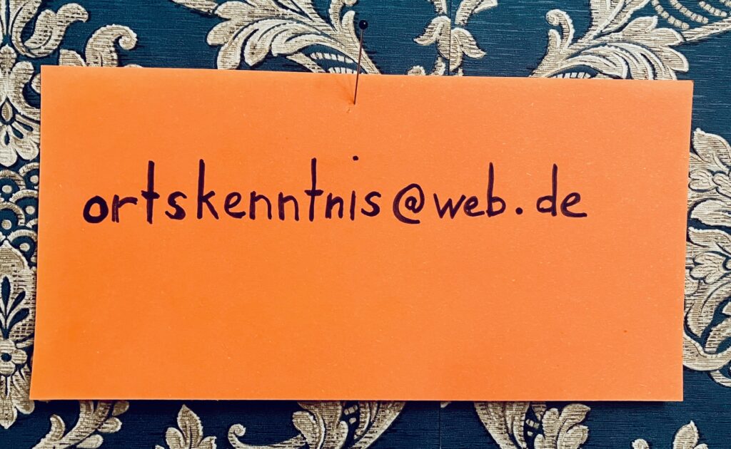 Orangene Karte mit einer E-Mail-Adresse auf blau-golden gemusterter Tapete befestigt