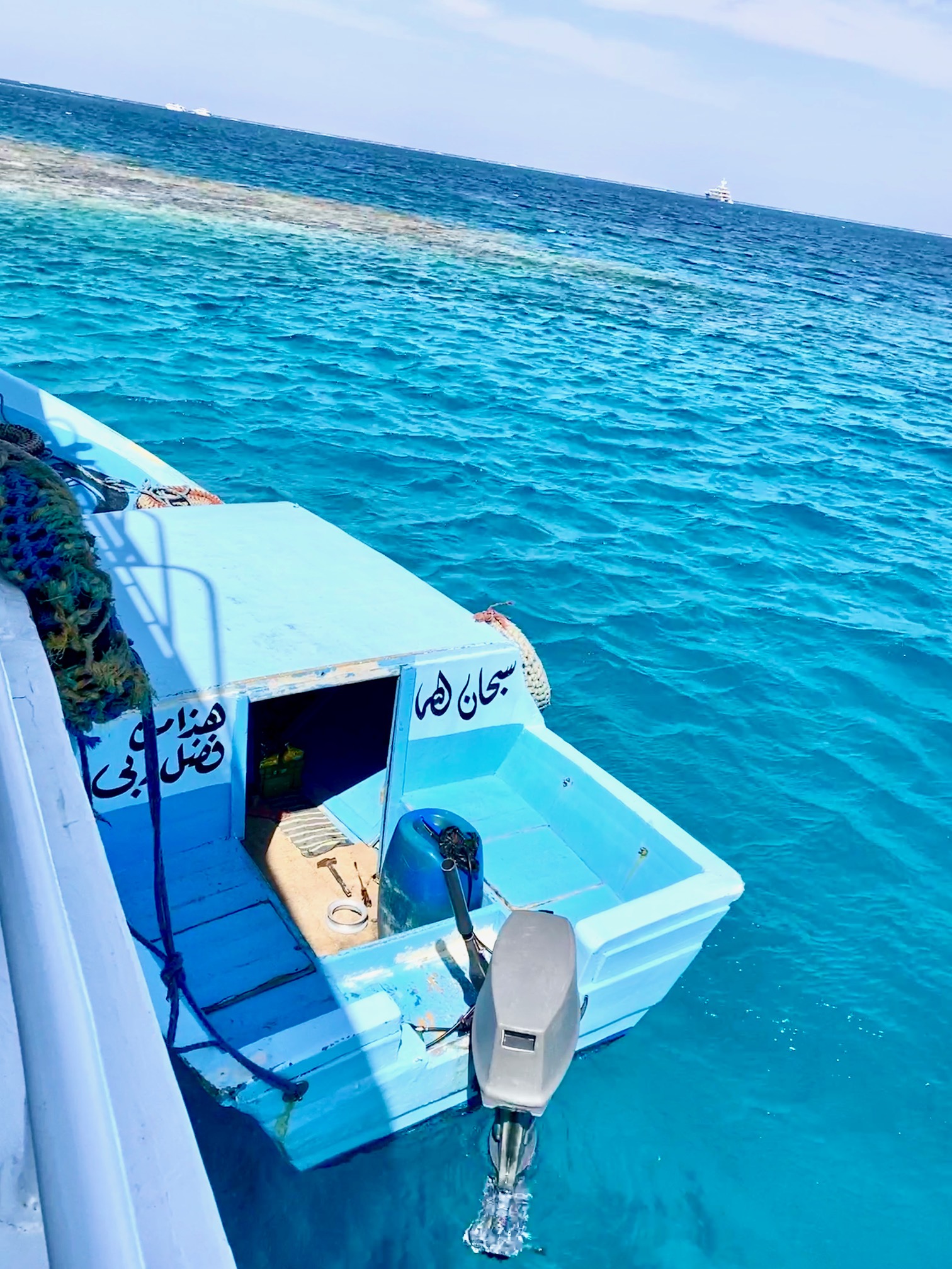 Blaues Motorboot mit arabischer Schrift am Heck auf klarem, türkisfarbenem Meerwasser