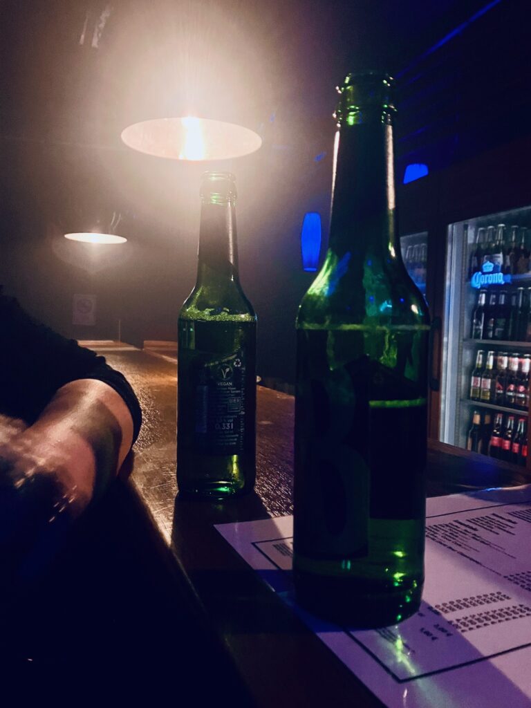 Zwei grüne Bierflaschen auf einem dunklen mit gedämpfter Beleuchtung und Kühlschrank im Hintergrund