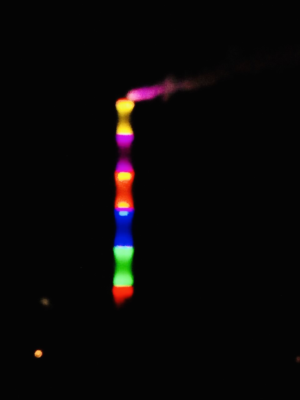 Vertikal angeordnete, unscharfe Lichtpunkte in den Farben Gelb, Pink, Rot, Blau, Grün und Rot vor schwarzem Hintergrund. Das Bild zeigt eine künstlerische Nachtaufnahme der künstlerischen Lichtinstallation am Kamin des Heizkraftwerks Chemnitz-Nord