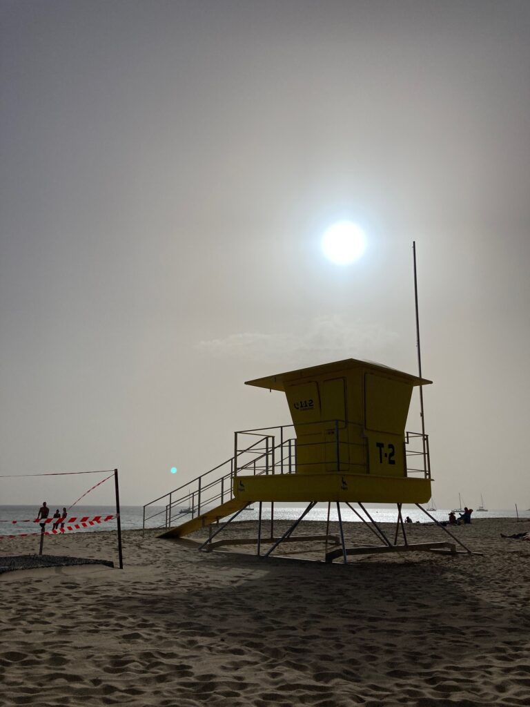 Gelber Rettungsturm am Strand im starken Gegenlicht mit heller Sonne, im Hintergrund Meer