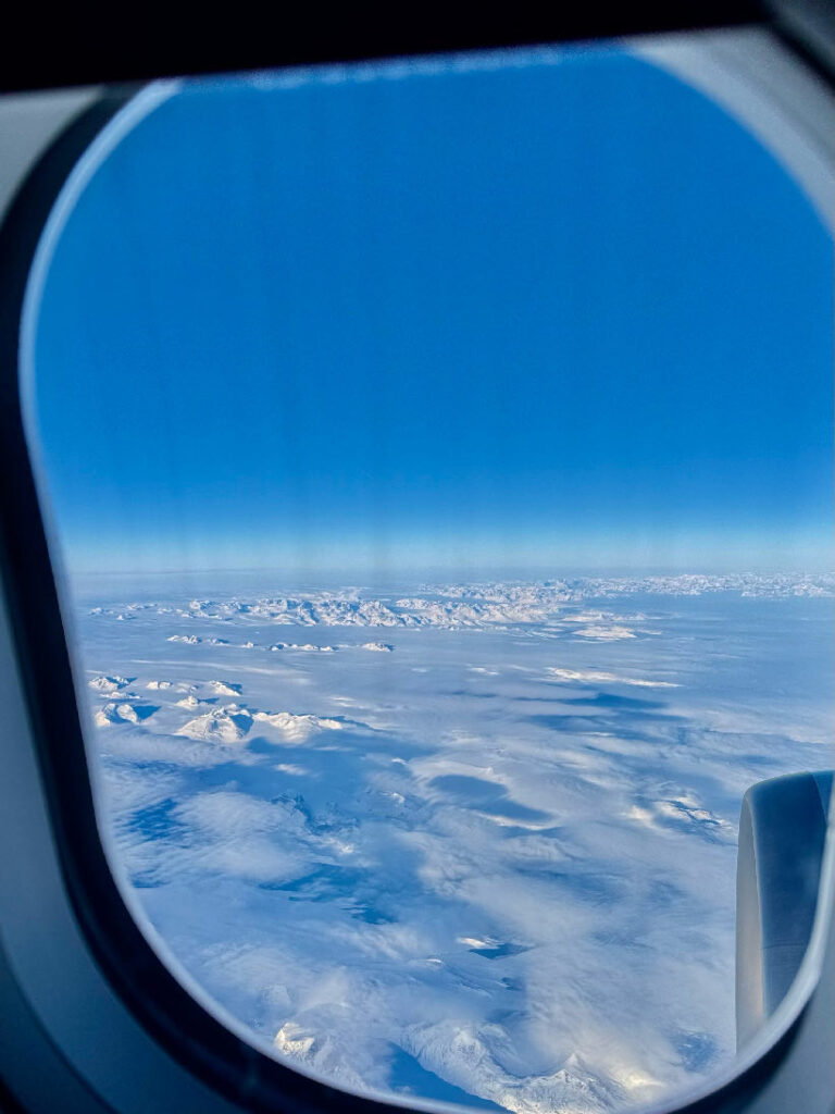 Blick aus einem Flugzeugfenster auf schneebedeckte Berge unter klarem blauem Himmel