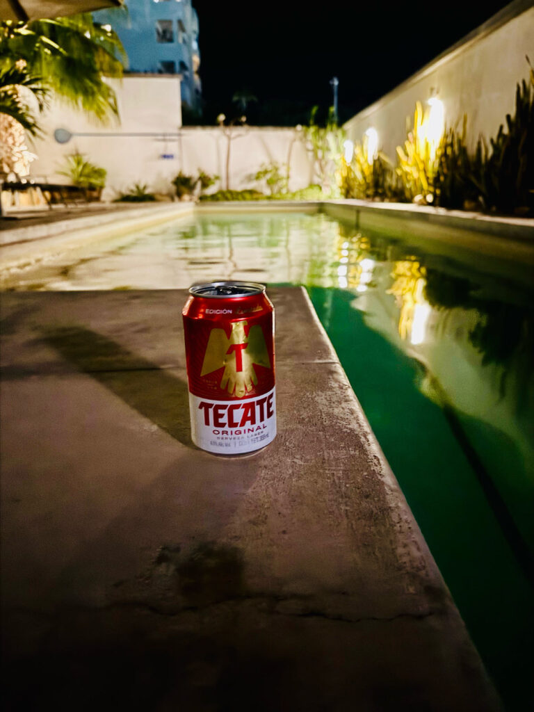 Eine Bierdose mit der Aufschrift Tecate steht auf dem Rand eines beleuchteten Schwimmbeckens bei Nacht