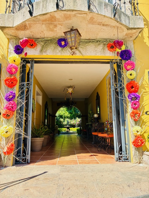 Bogenförmiger Hauseingang mit bunter Blumendekoration aus roten, gelben, orangefarbenen und violetten Blüten