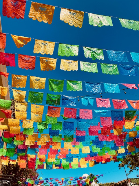 Mehrere Reihen bunter, rechteckiger Papiergirlanden mit ausgeschnittenen Mustern hängen vor blauem Himmel