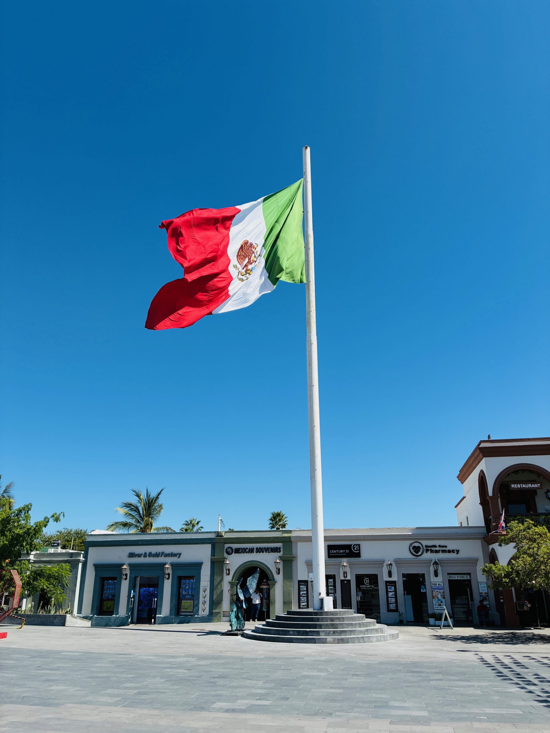 Große mexikanische Flagge weht auf einem Platz vor tiefblauem Himmel