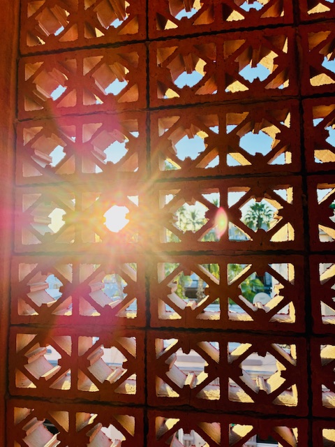 Sonnenlicht scheint durch ein braunes, geometrisch gemustertes Ziegelmauerwerk mit quadratischen Öffnungen