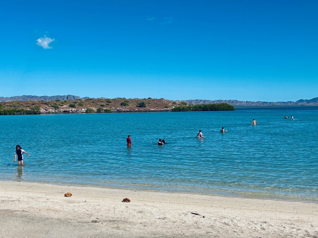 Mehrere Personen gehen und schwimmen vom Strand im Gänsemarsch ins tiefblaue Meer stehen und schwimmen in einer Reihe im tiefblauen Meer unter blauem Himmel