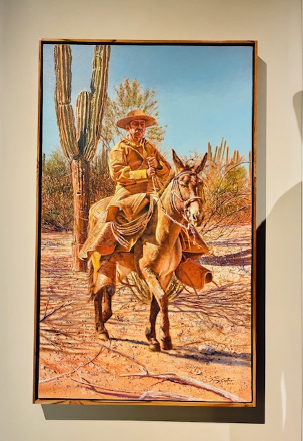 Gemälde eines Reiters in gelber Kleidung und breitkrempigem Hut auf einem Esel in einer Wüstenlandschaft mit Kakteen
