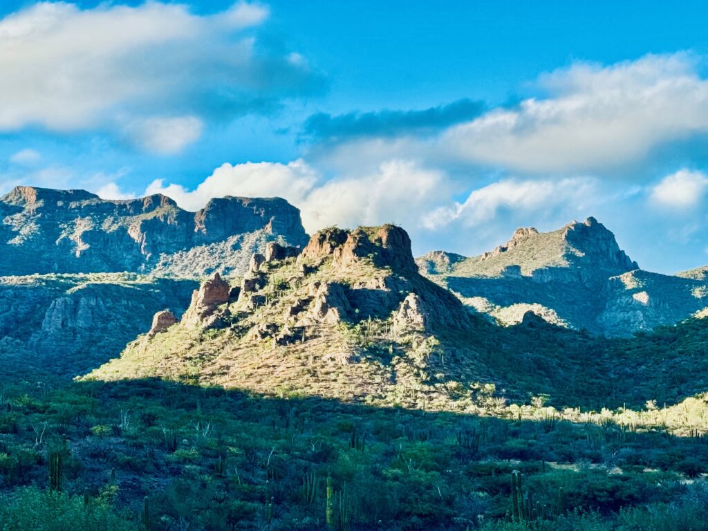 Berglandschaft mit zerklüfteten Gipfeln und karger Vegetation unter blauem Himmel mit wenigen Wolken