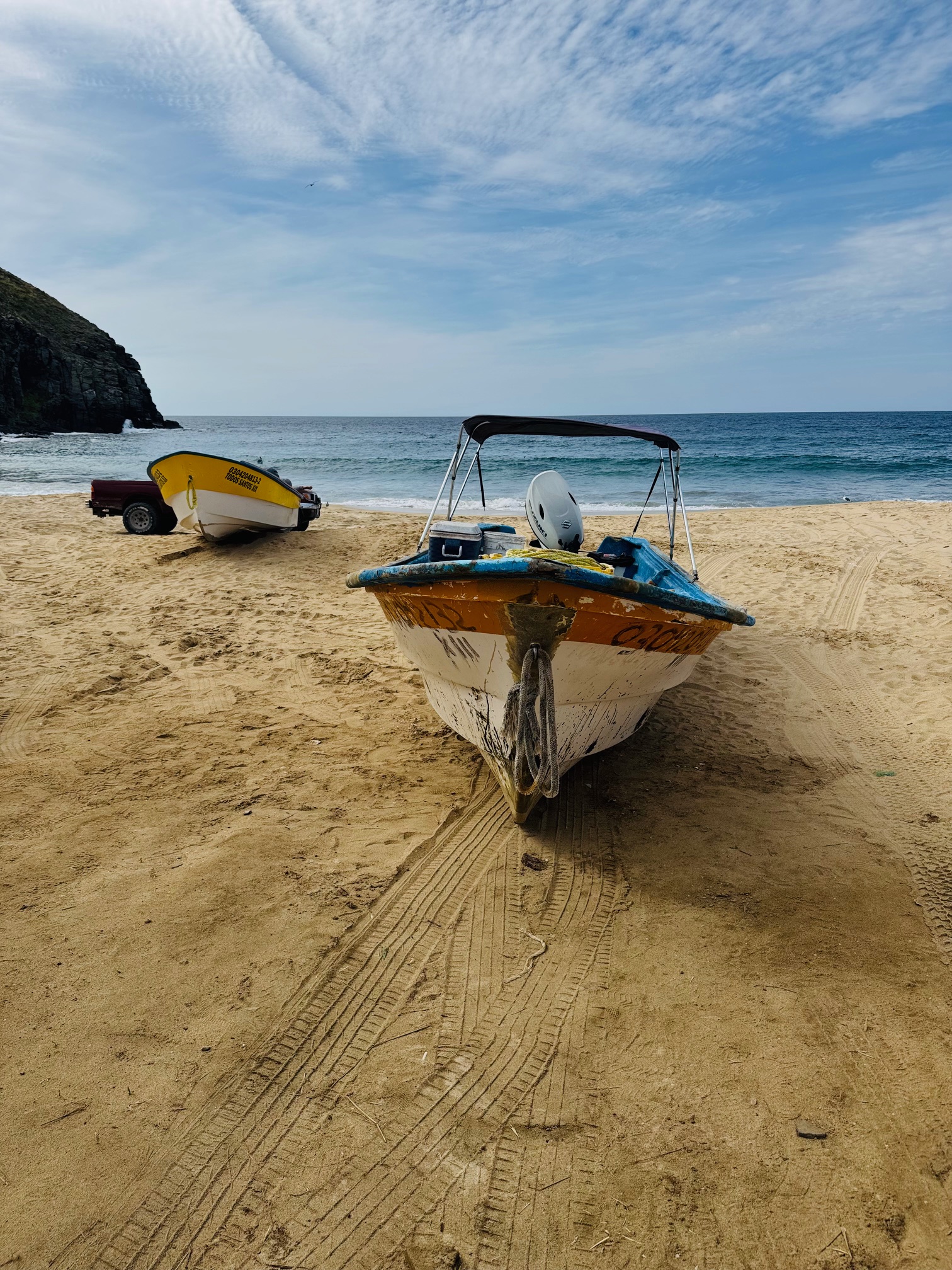 Zwei kleine Boote stehen auf sandigem Strand, eines vorne mit Motor und Überdach, das andere mit gelbem Rumpf