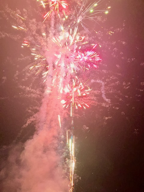 Mehrere bunte Feuerwerkskörper explodieren am Nachthimmel, Rauch steigt nach oben