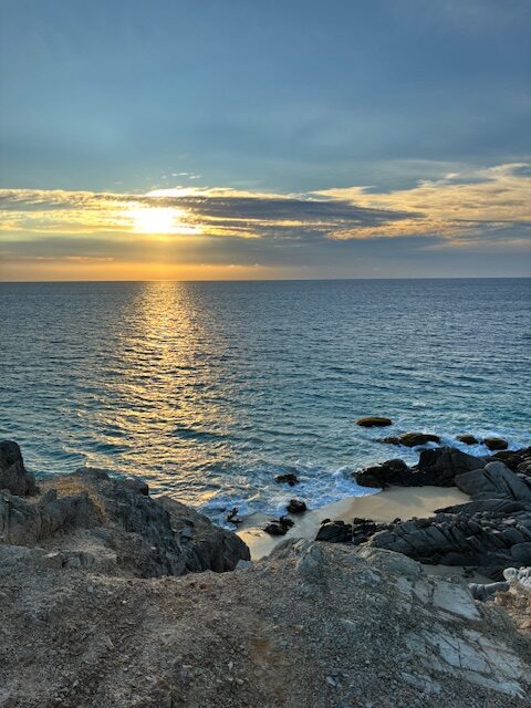 Sonnenuntergang über dem Meer mit bewölktem Himmel und felsiger Küste im Vordergrund