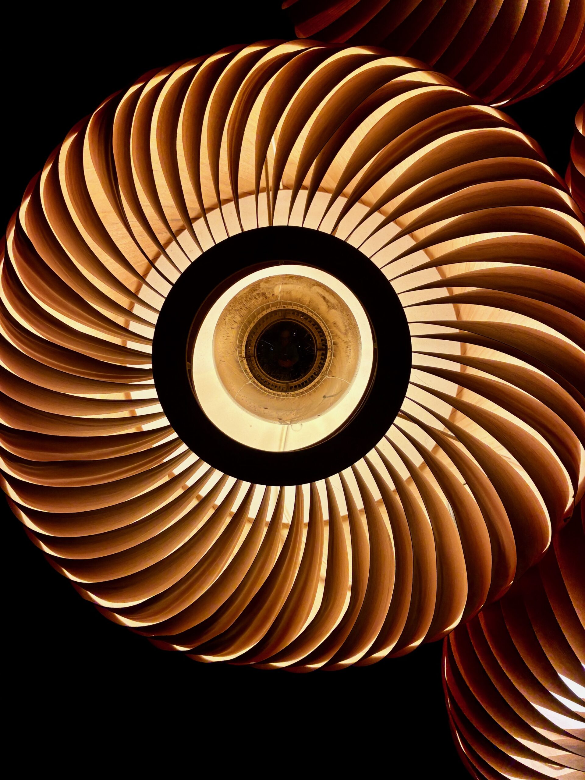 Nahaufnahme einer runden Lampe mit spiralförmig angeordneten, gebogenen Lamellen in warmem Braunton