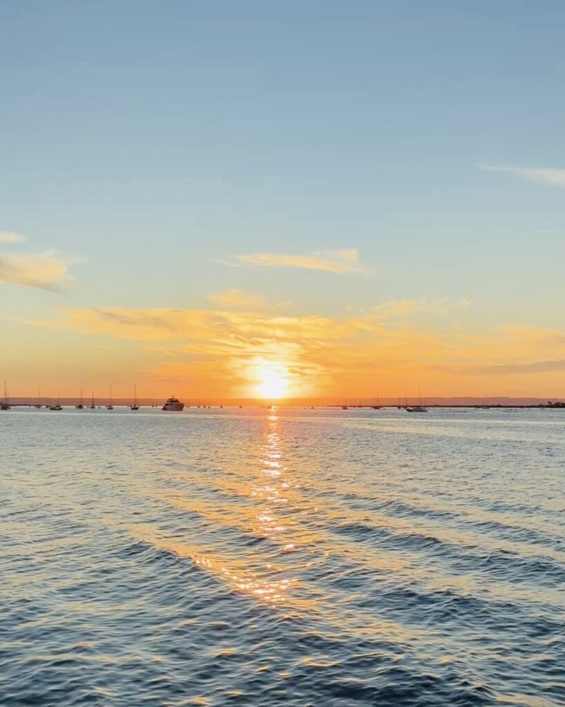 Sonnenuntergang über ruhigem Meer mit mehreren Segelbooten am Horizont und orangefarbenem Himmel