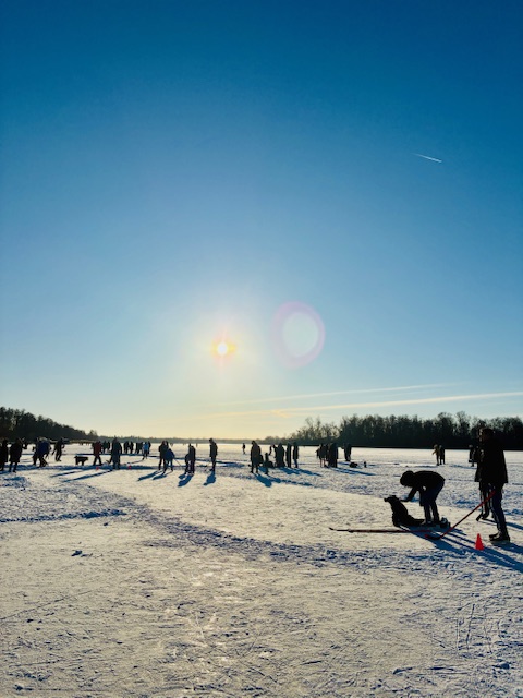 Menschen auf einer zugefrorenen Eisfläche bei tiefstehender Sonne mit langen Schatten und klarem Himmel.