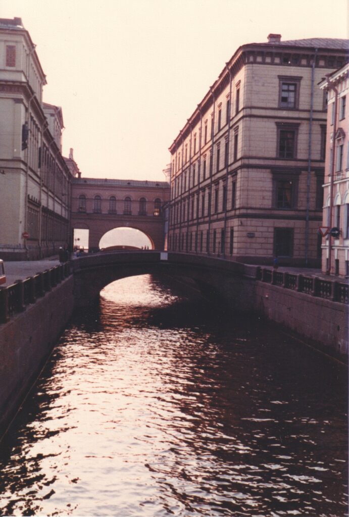 Kanal mit Brücke und historischen mehrstöckigen Gebäuden auf beiden Seiten im Gegenlicht unter dunstigem Himmel. Historische Analogaufnahme