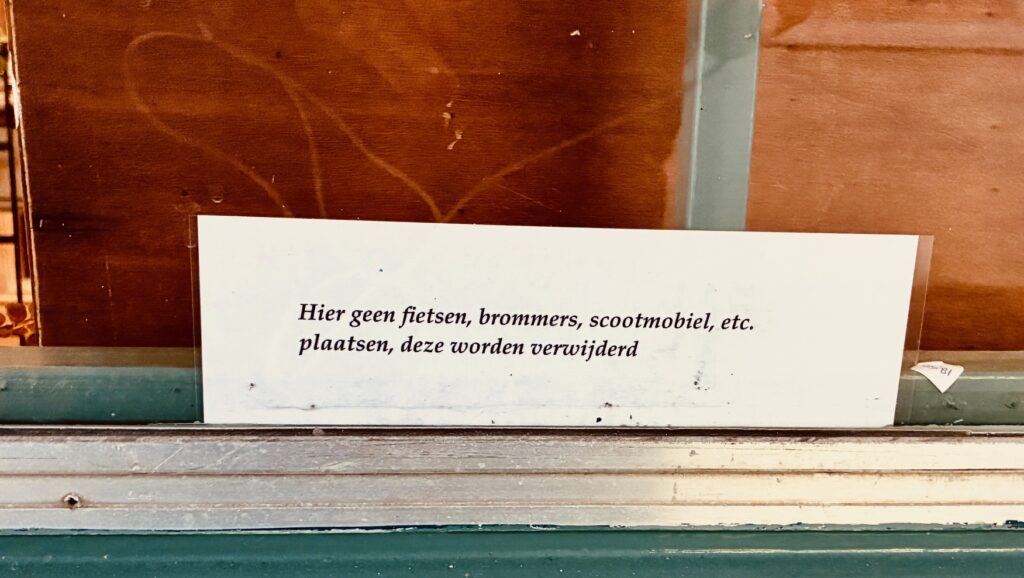 Weißes Schild mit niederländischem Text auf einer Holz- und Glasfläche