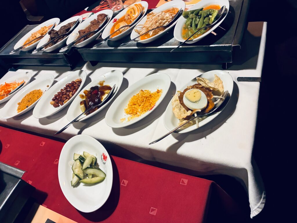 Viele kleine weiße Servierteller mit verschiedenen Speisen auf einem weißen Tisch mit rotem Tischtuch