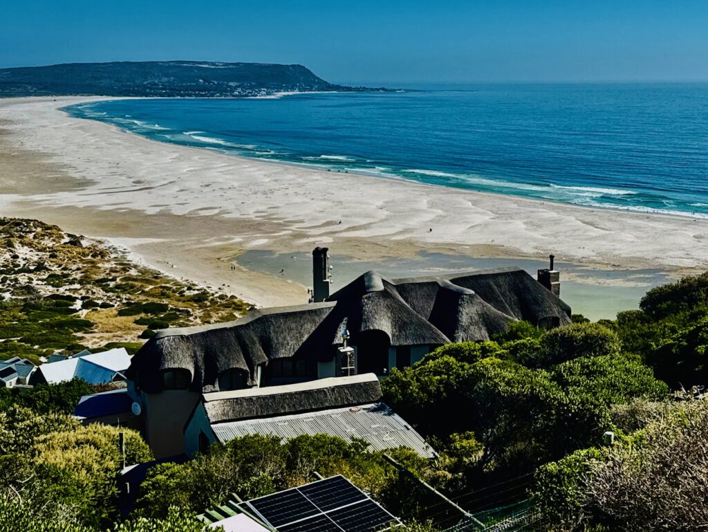 Haus mit Reetdach vor weitem Sandstrand und blauem Meer