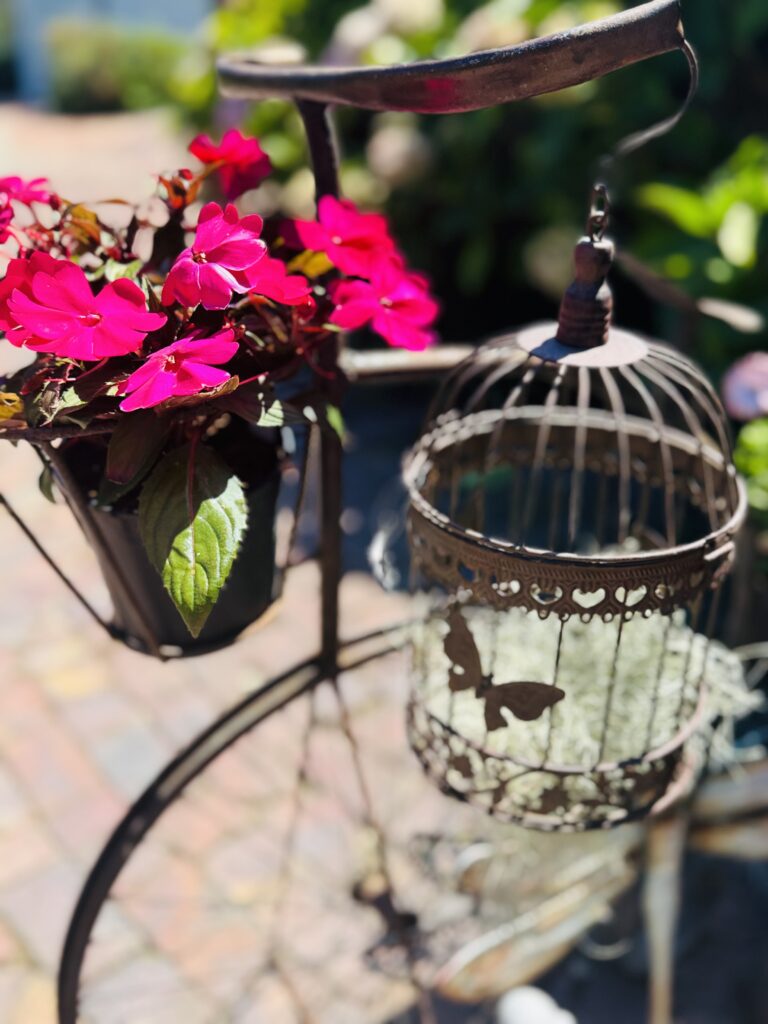 Nahaufnahme einer hängenden Metalllaterne mit Schmetterlingsmotiv neben einem Topf mit leuchtenden Blüten