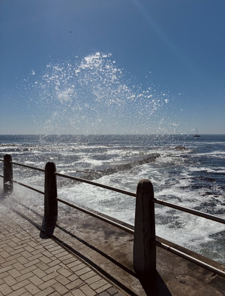 Wellen spritzen gegen eine Uferpromenade mit Geländer unter klarem Himmel