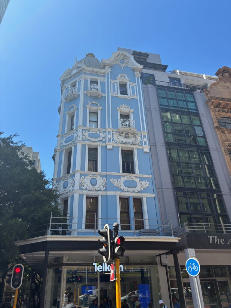 Mehrstöckiges Gebäude mit hellblauer Fassade und weißem Stuck neben einem modernen Glasgebäude unter blauem Himmel