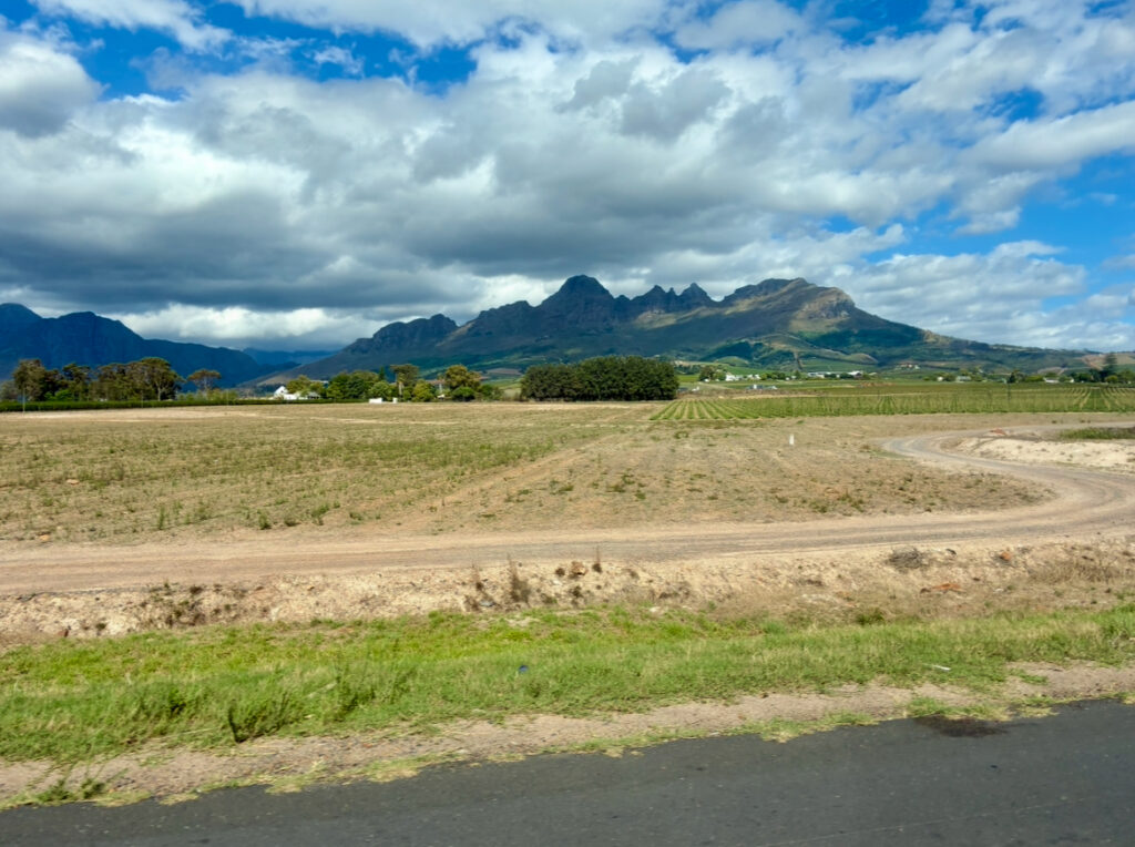 Landschaft mit Ackerfläche, gewundenem Feldweg und Bergen im Hintergrund unter bewölktem Himmel