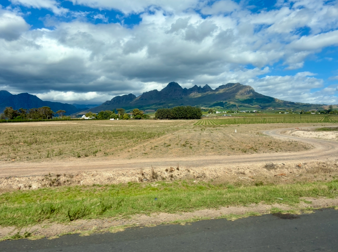 Landschaft mit Ackerfläche, gewundenem Feldweg und Bergen im Hintergrund unter bewölktem Himmel