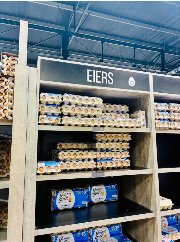 Regal mit mehreren Eierschachteln aus Pappe, darüber ein Schild mit der Aufschrift 'EIERS' und einem Eier-Symbol