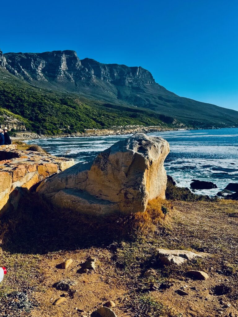 Felsformation am Küstenrand mit Meer und bewaldetem Gebirge im Hintergrund