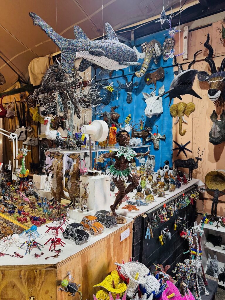 Bunte Drahtskulpturen verschiedener Tiere und Figuren, darunter Haie, Vögel, ein tanzender Mensch und Autos, auf einem Marktstand