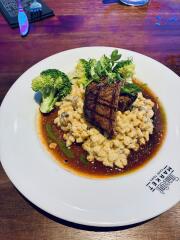 Teller mit gebratenem Fleisch auf gekochtem Weizen und Brokkoli, garniert mit frischen Kräutern auf Holztisch