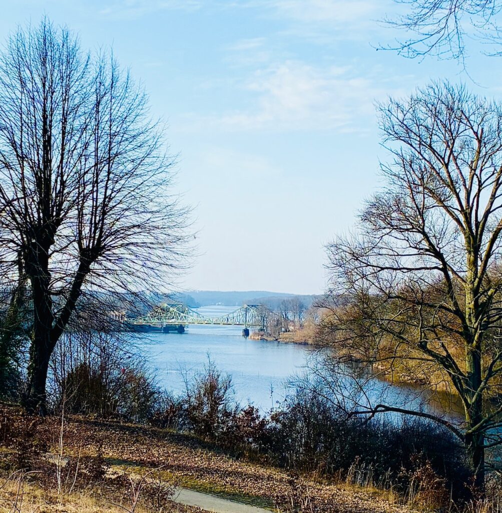 Blick auf die Glienicker Brücke, umgeben von kahlen Bäumen und vorfrühlingshafter Vegetation unter blassblauem Himmel