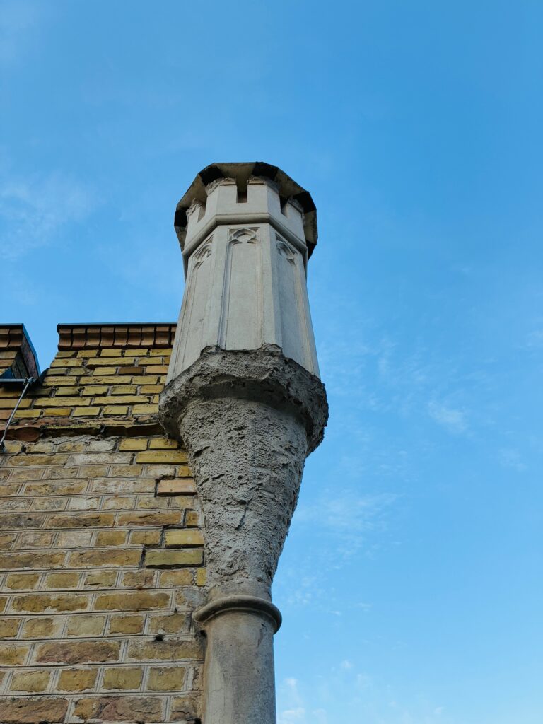 Schornstein im gotischen Stil mit verputztem Sockel an gelber Backsteinwand vor blauem Himmel