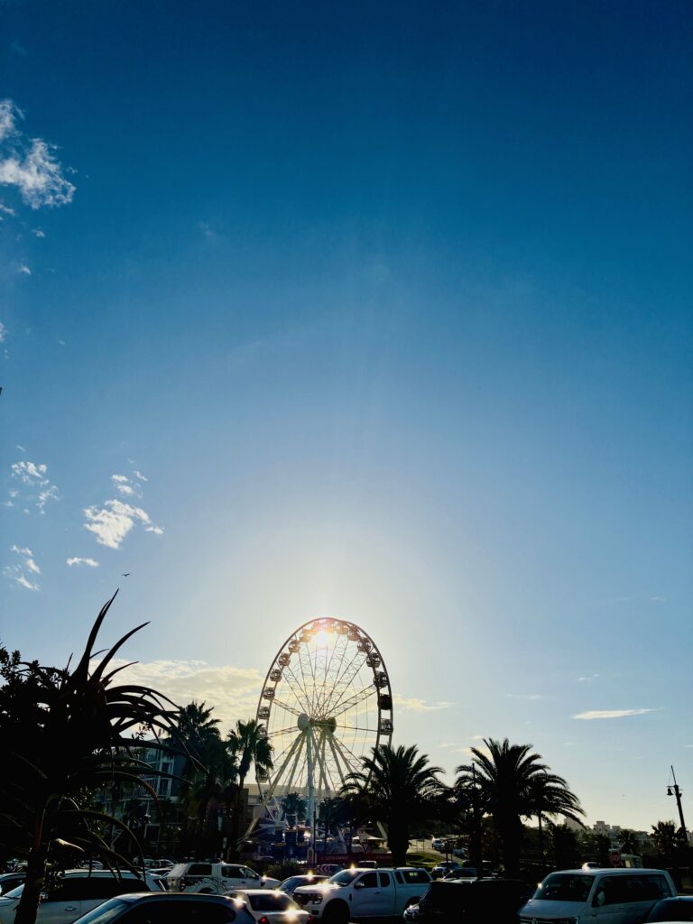Riesenrad vor tiefblauem Himmel mit Sonne dahinter und Palmen im Vordergrund