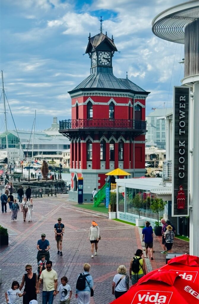 Rotes historisches Gebäude an der Victoria & Albert Waterfront in Kapstadt mit Passanten unter blauem Himmel mit freundlichen Wolken